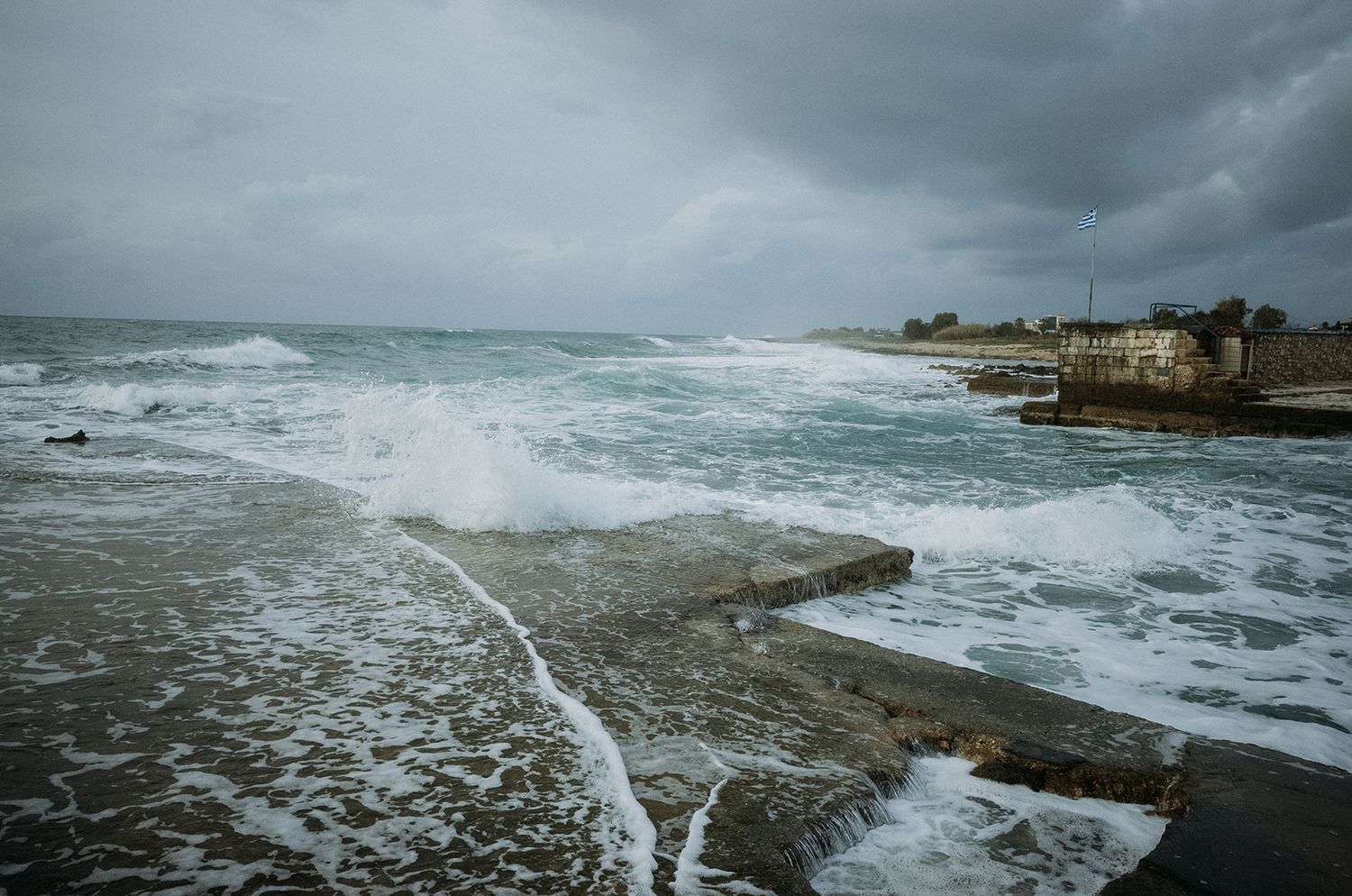 Stormy seascape with crashing waves against concrete pier during overcast weather.
