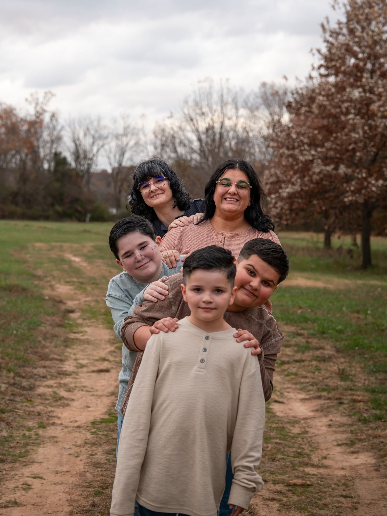 A group stands together on a dirt path through an autumn field, sharing warm embraces and smiles.