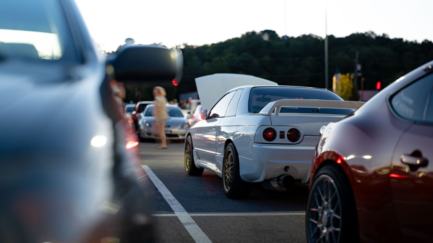 Row of modified sports cars parked at dusk during a car meet.