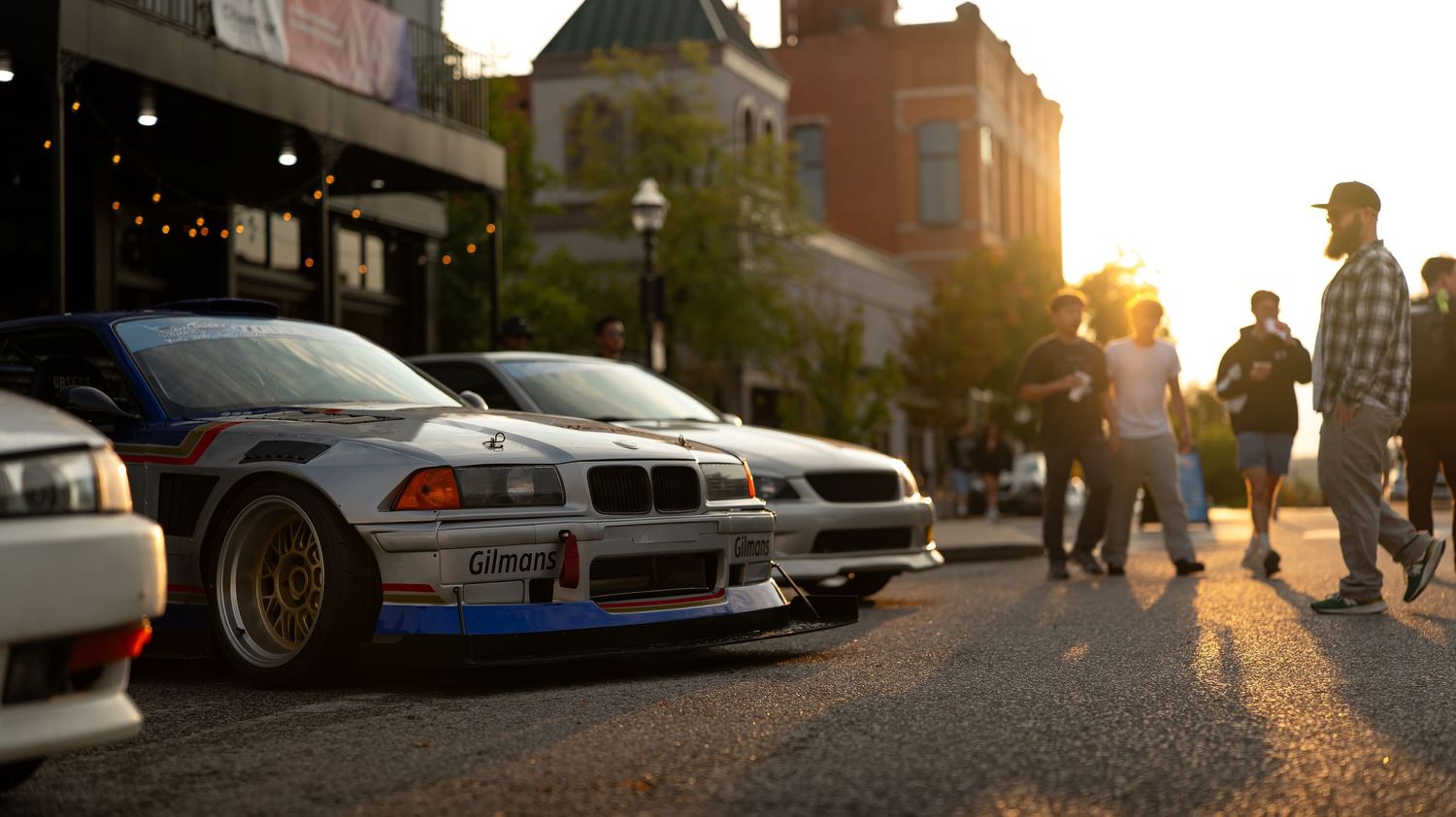 Urban street scene with cars parked along buildings during sunset hours.