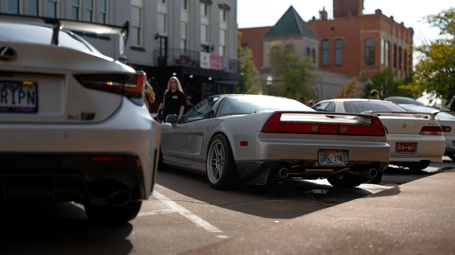 Row of cars parked along a street with modern buildings in the background.