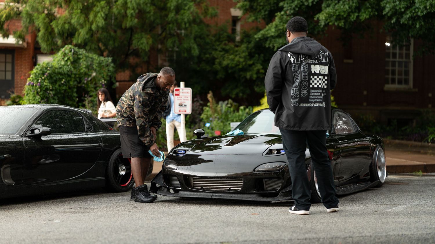 Car enthusiasts gathered in a parking lot with modified vehicles.