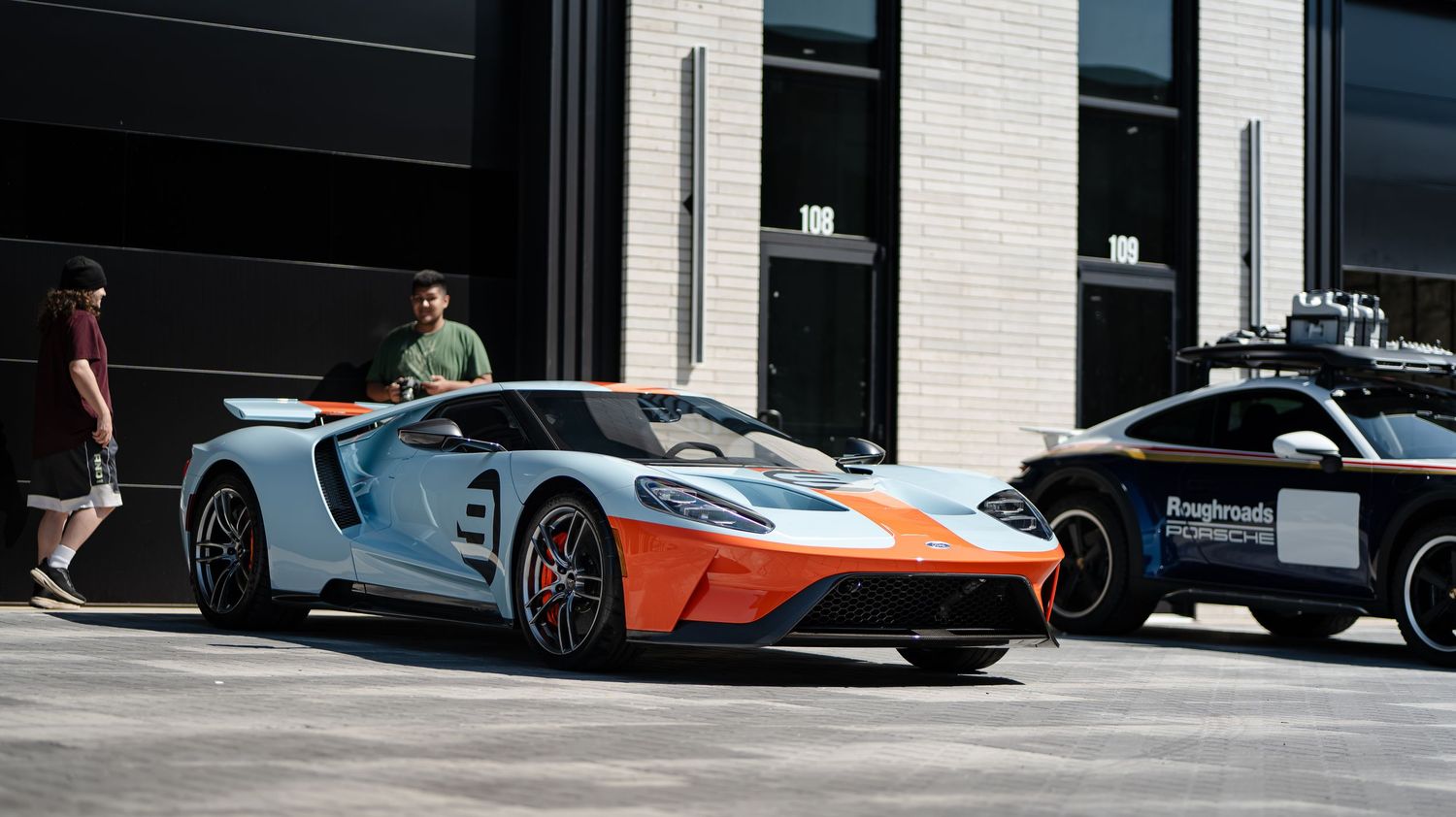 Modern luxury vehicles displayed outside white building with glass windows.