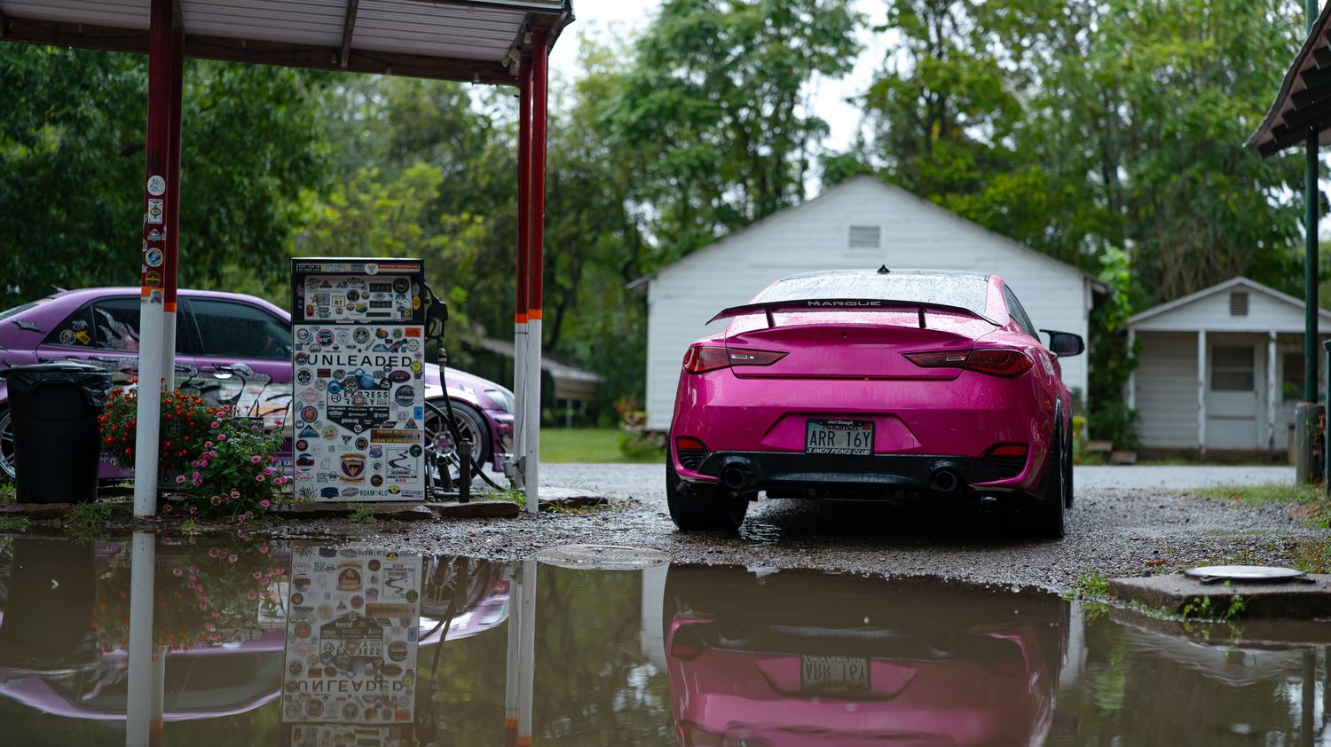 Custom cars parked under a red-roofed structure with water reflections visible.