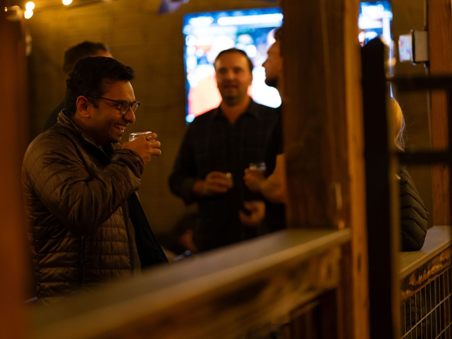 A crowded bar interior with patrons sitting at wooden counters illuminated by warm lighting.