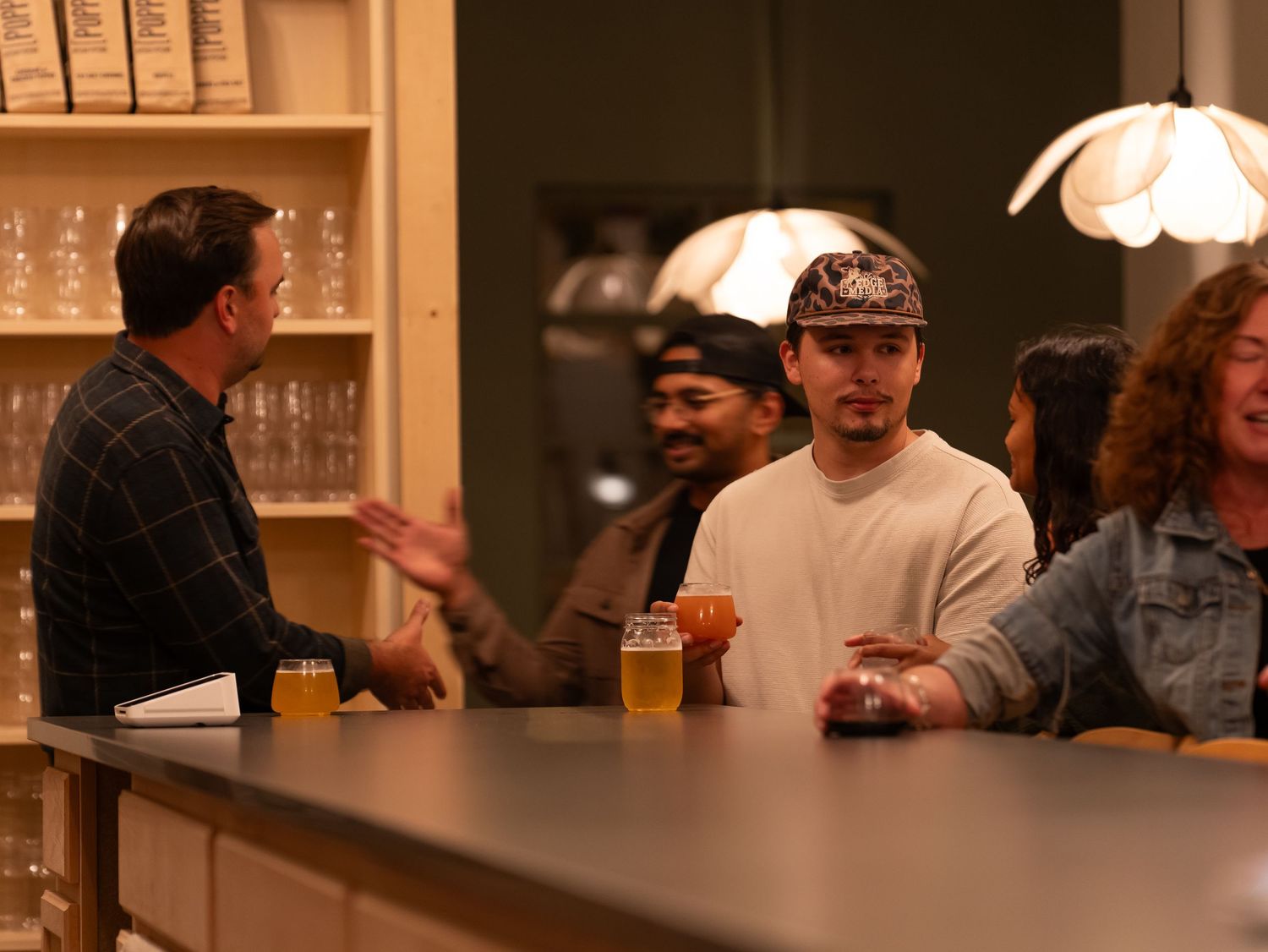 People gathered at a bar counter with drinks while engaging in conversation under warm lighting.