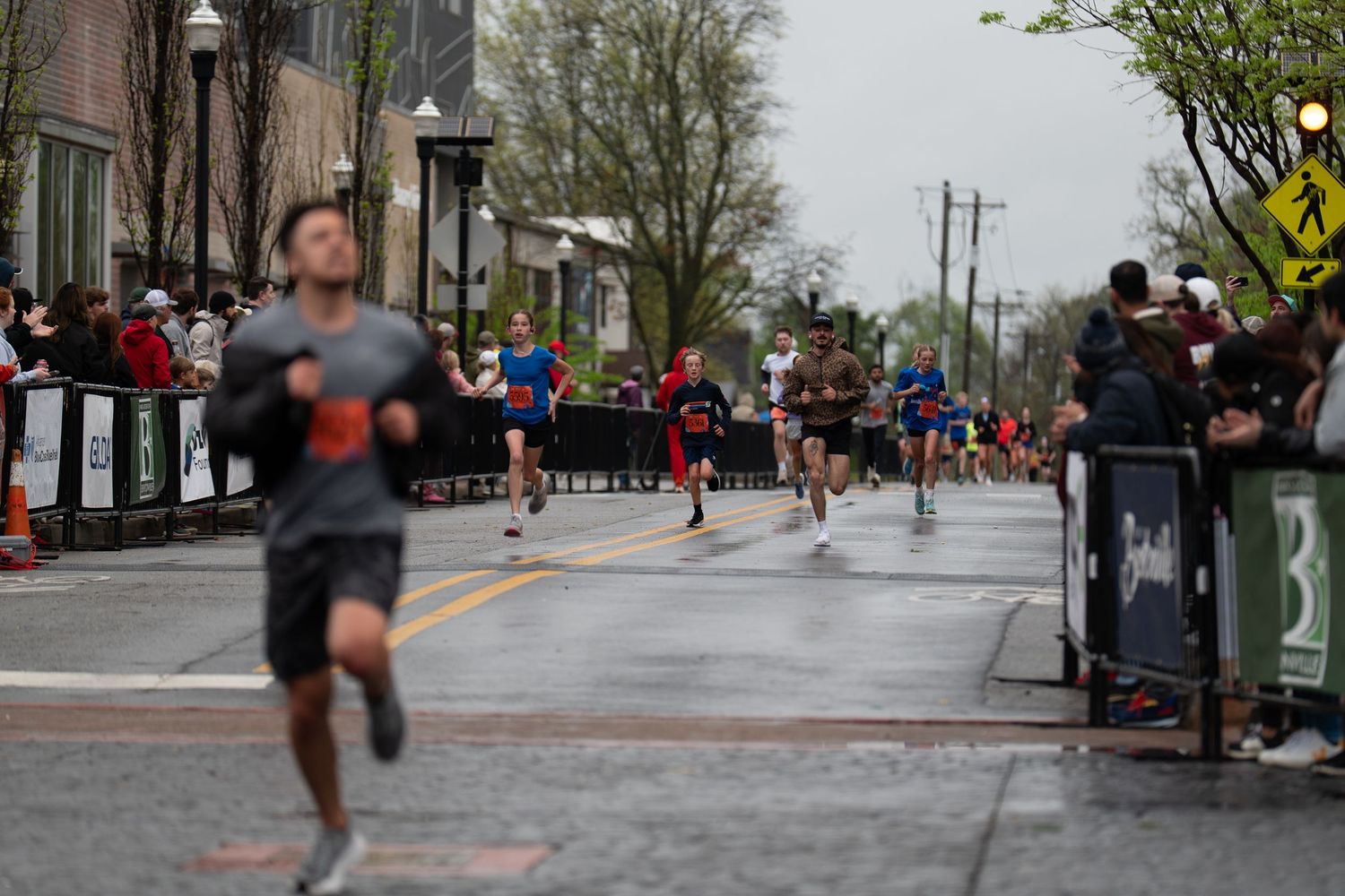 Runners competing in a city street marathon on a cloudy spring day, with spectators lining the barricades.