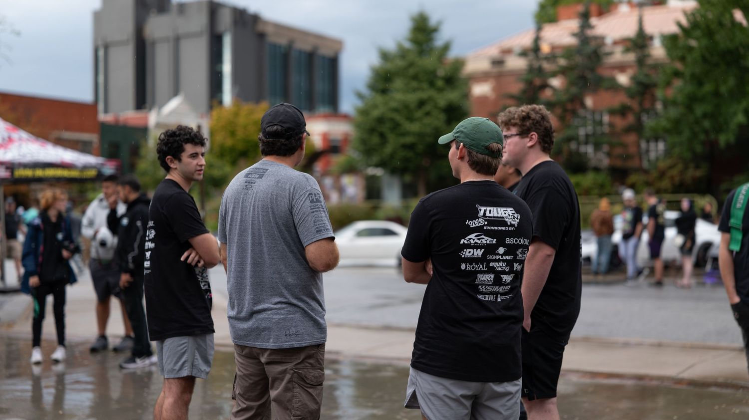 People gathering at an outdoor car meet with modified vehicles on display.