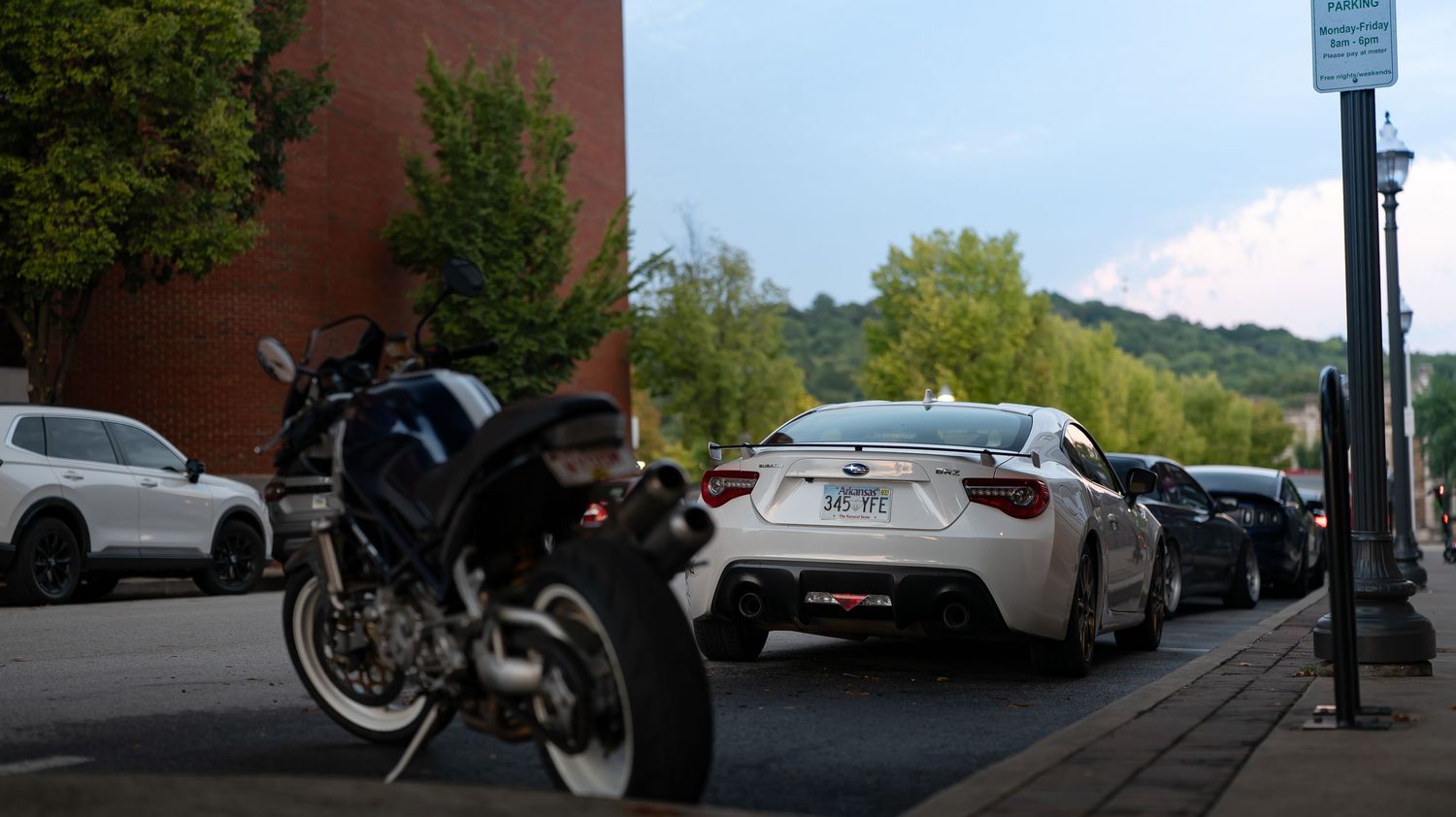 Panoramic view of a city street with brick buildings and parked cars in the evening light.