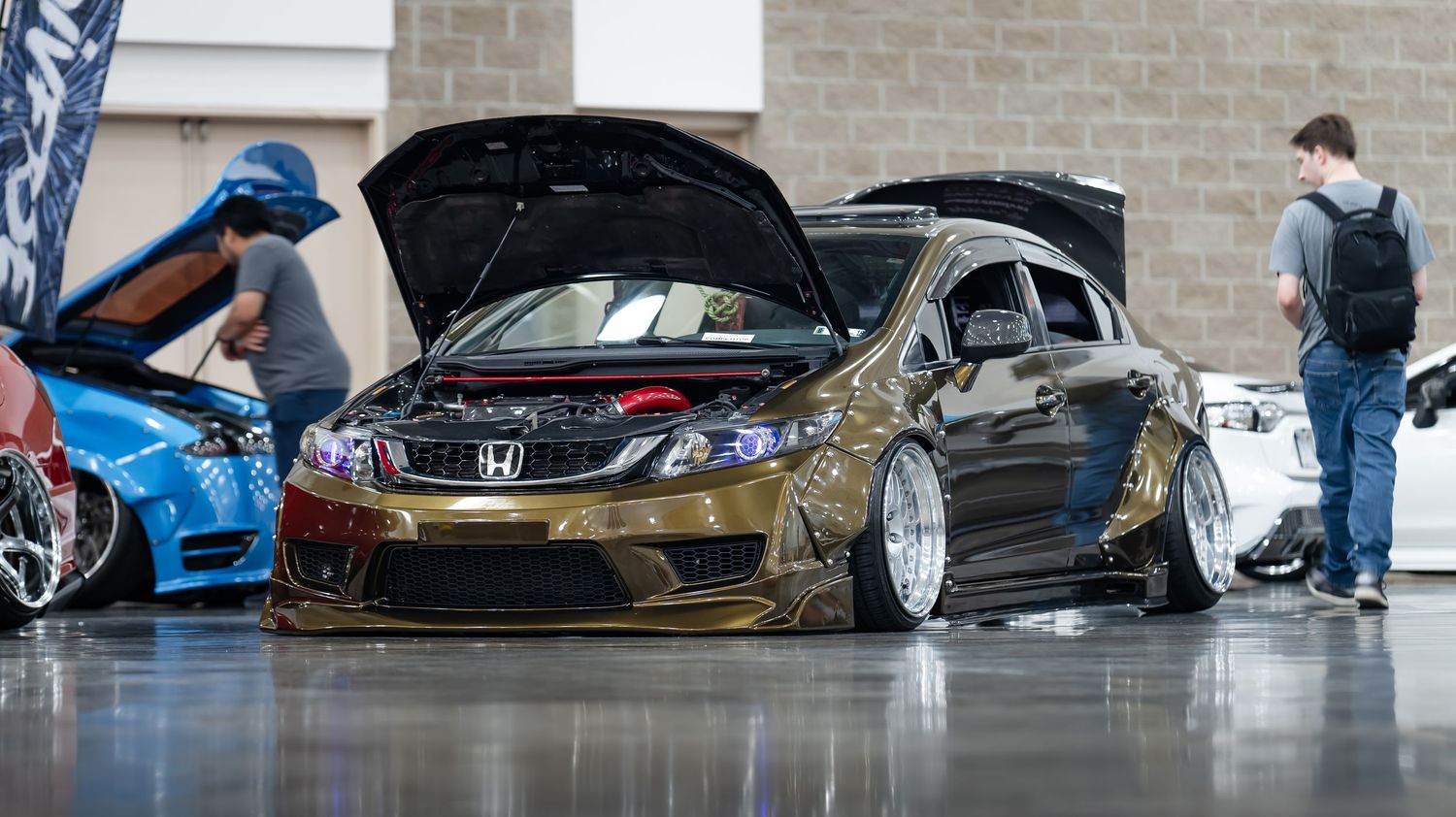 Modified import cars on display at an indoor car show with white walls.