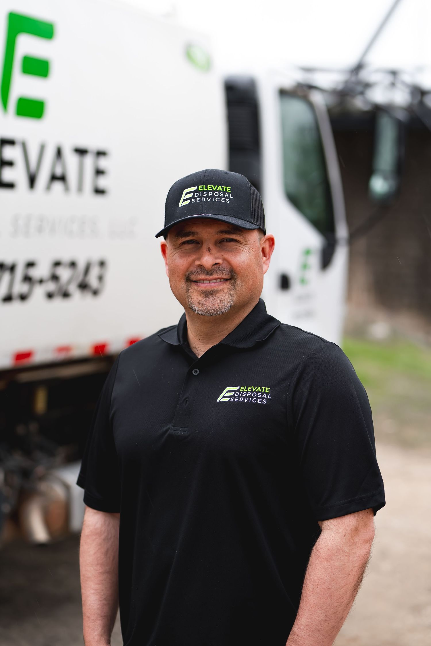 Person in company uniform and cap smiling near service vehicles.