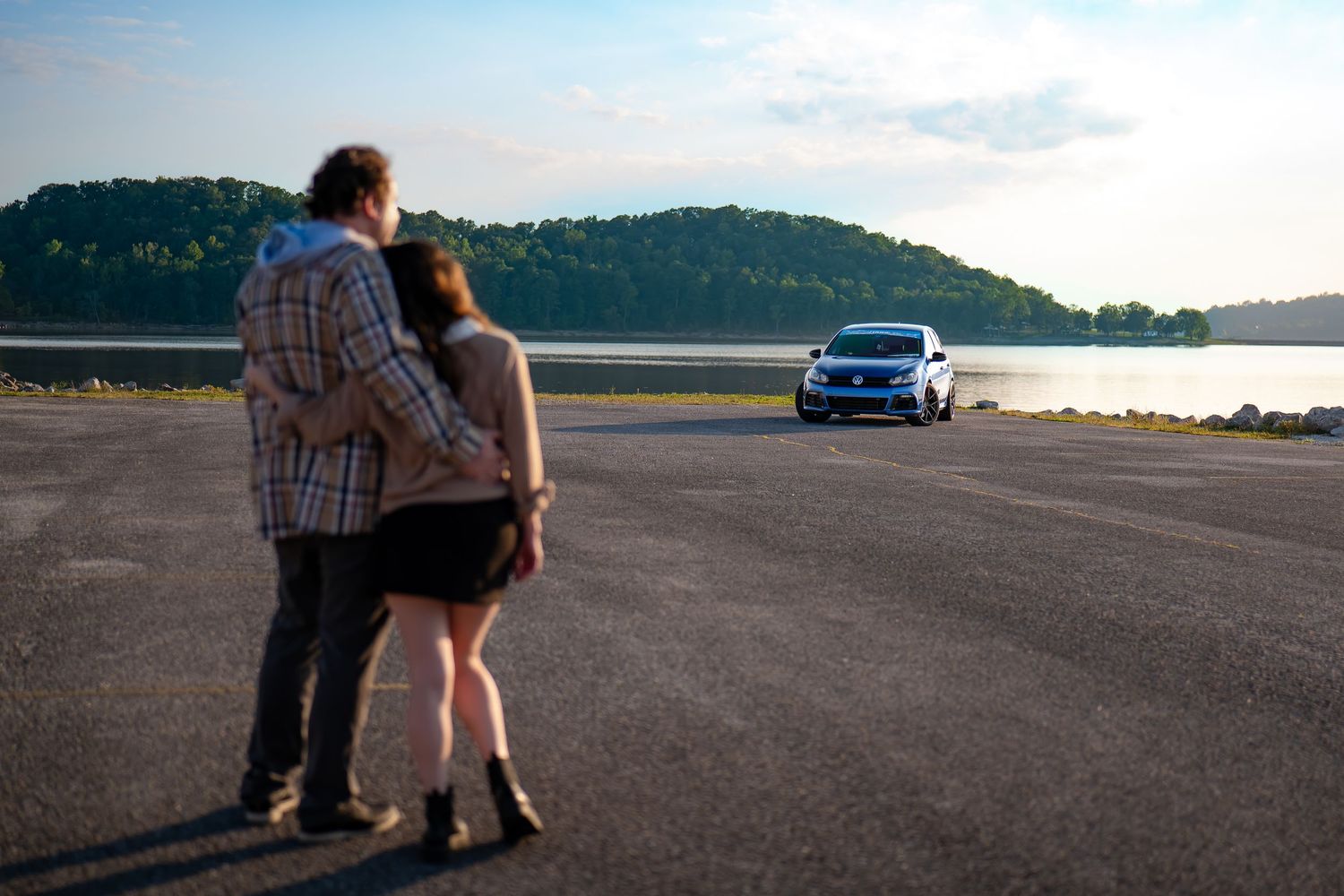 Couple sitting on pavement watching sunset with a blue car in the background.