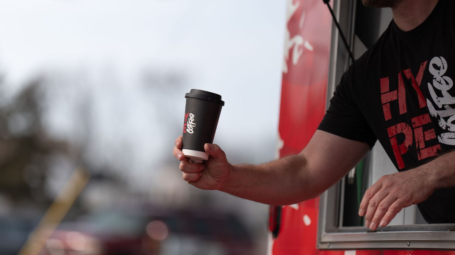 Hands exchanging dark coffee cups against a blurred exterior background.
