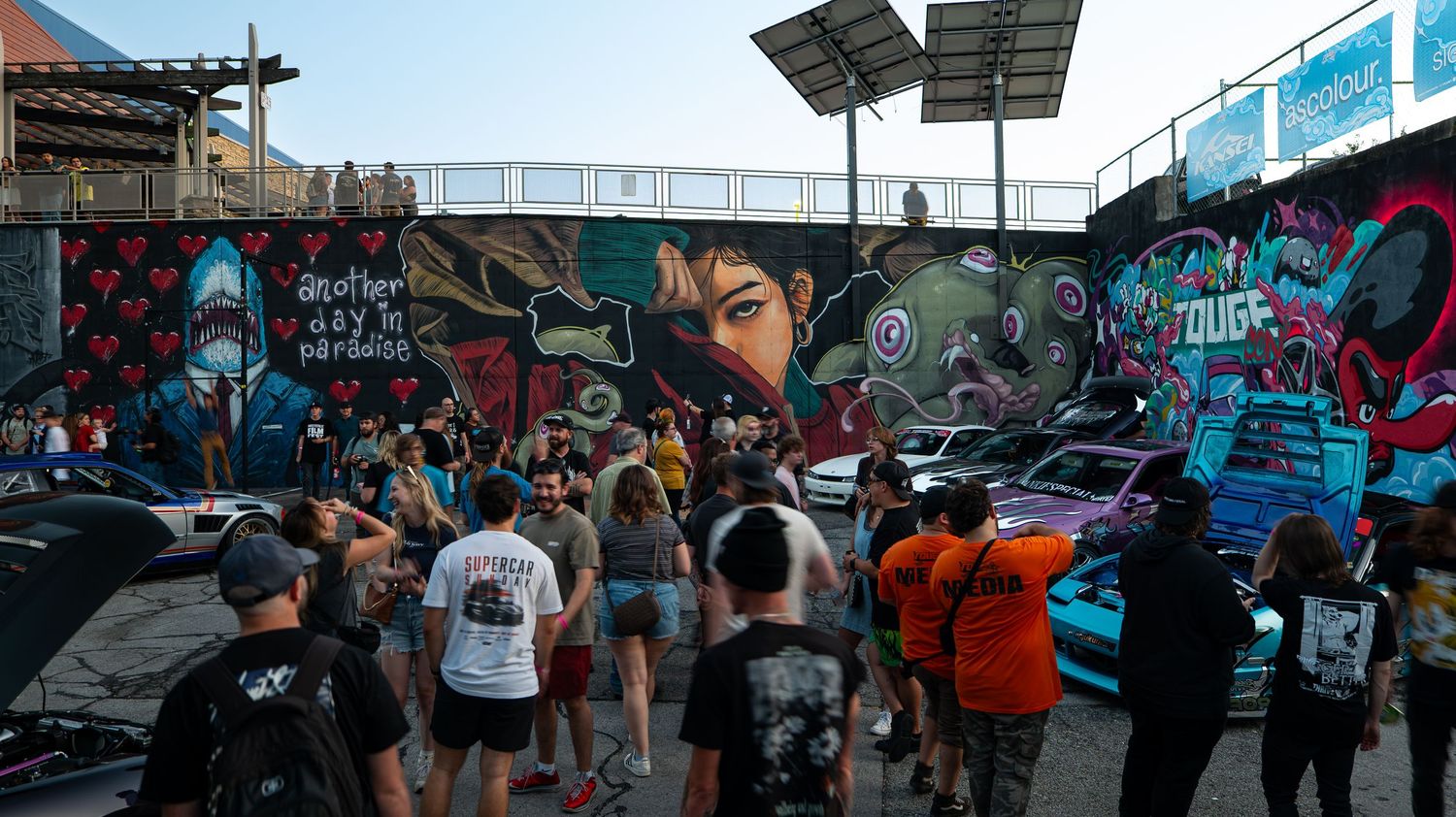 Outdoor event space with tents and crowds gathering near graffiti-covered walls.