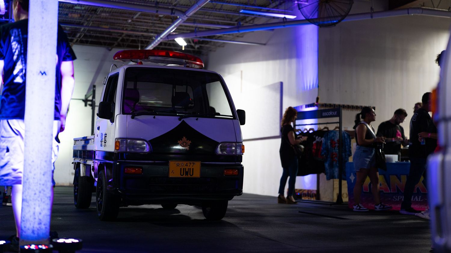 Large indoor space illuminated with blue LED lights showing parked vehicles and equipment.