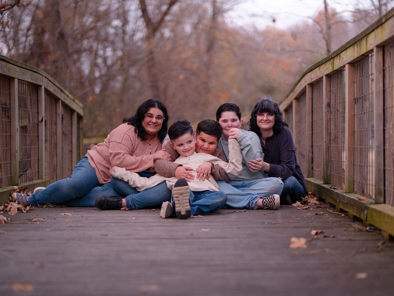 A group of people lying down on a wooden bridge during an autumn day in casual poses.