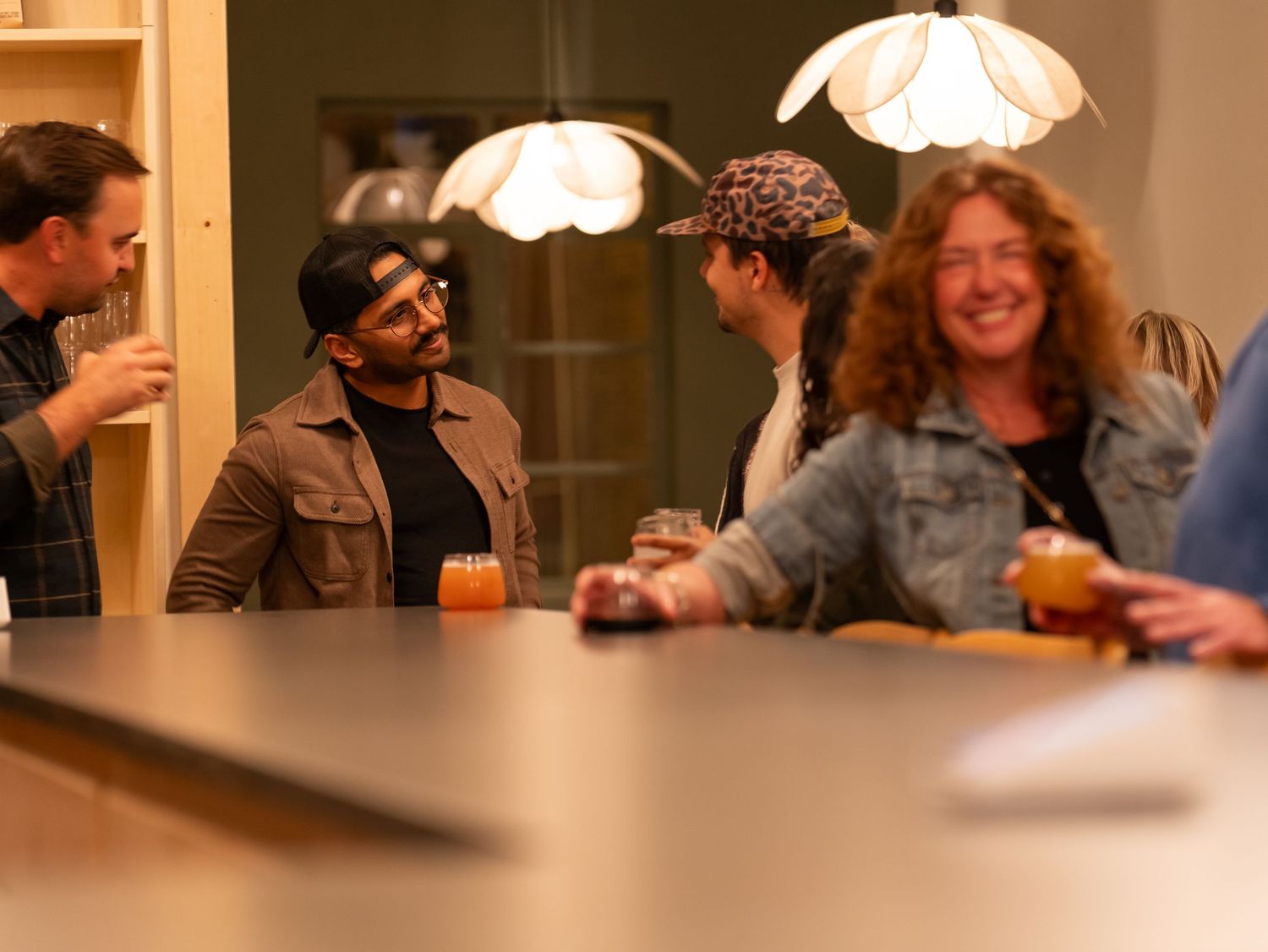 People gathered around tables in a warm, dimly lit room enjoying conversation and drinks together.