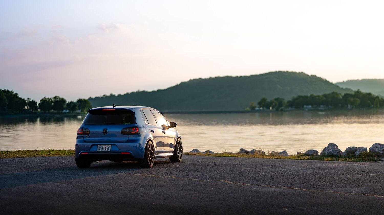 Panoramic landscape of cars parked near a lake during golden hour.