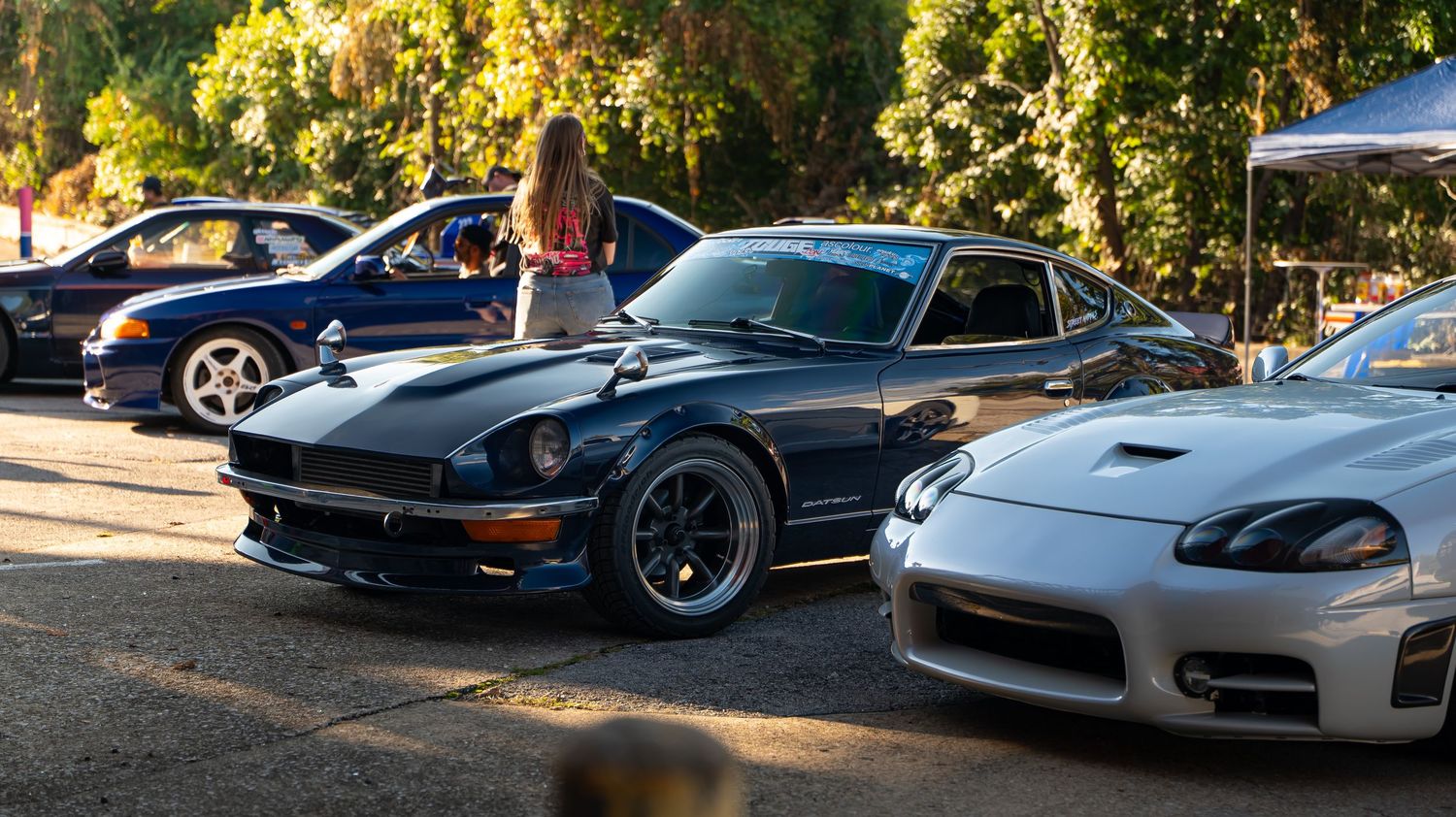 Row of sports cars parked at a car meet with autumn foliage in the background.