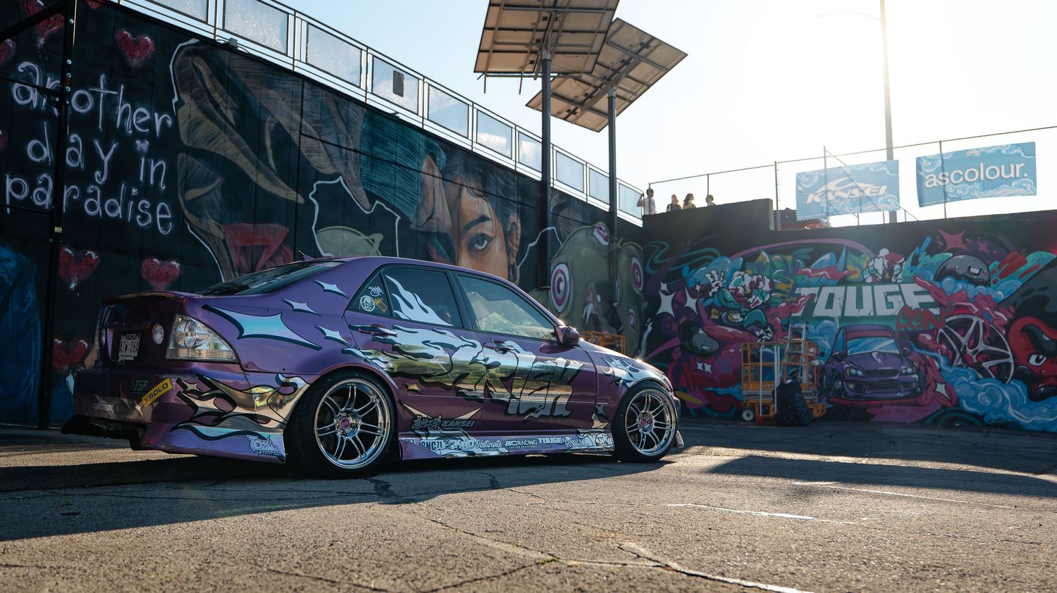 A panoramic view of parked cars against a wall with colorful graffiti art in an outdoor setting.