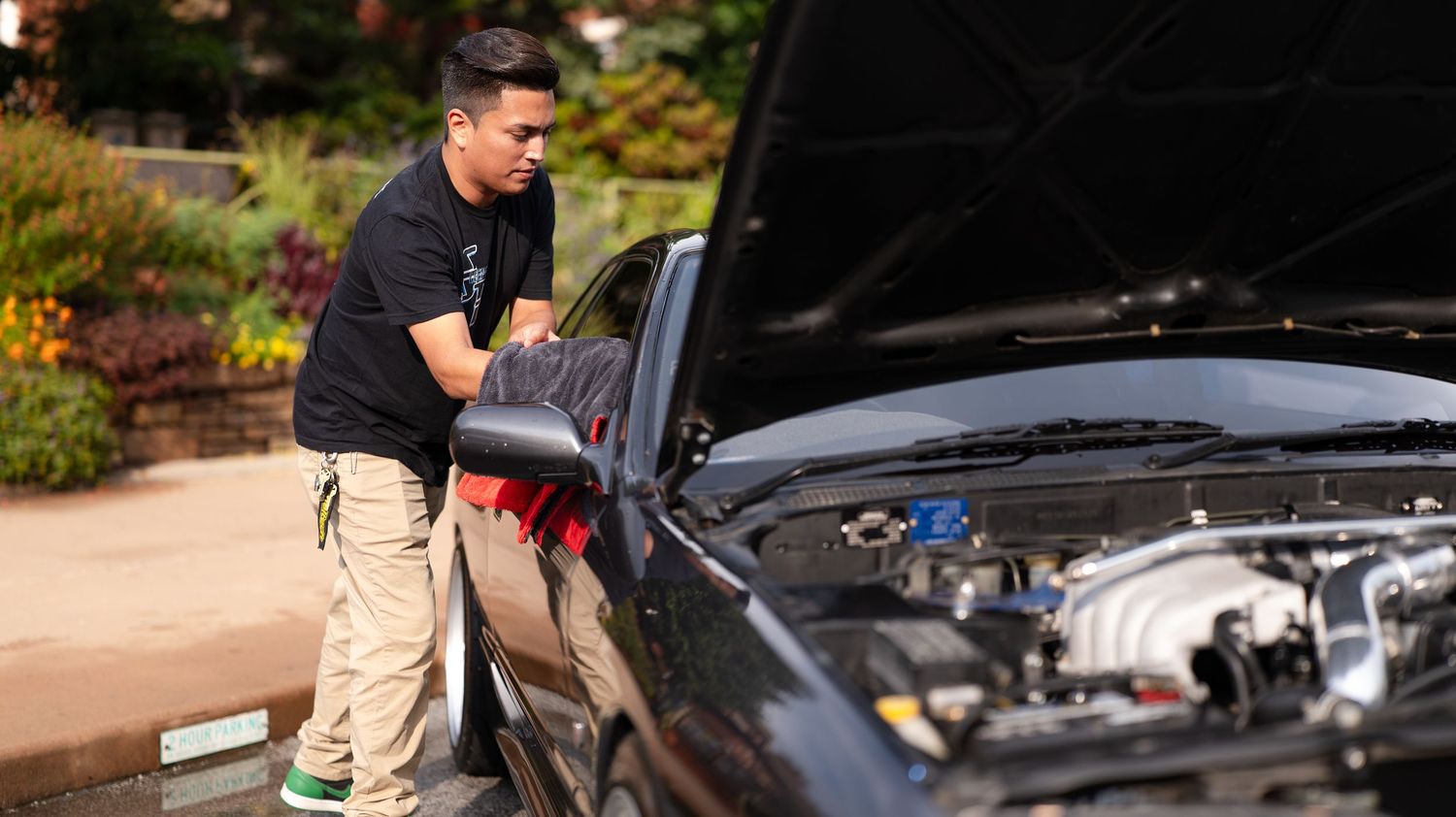Car enthusiasts examining under the hood of performance vehicles at a meetup.