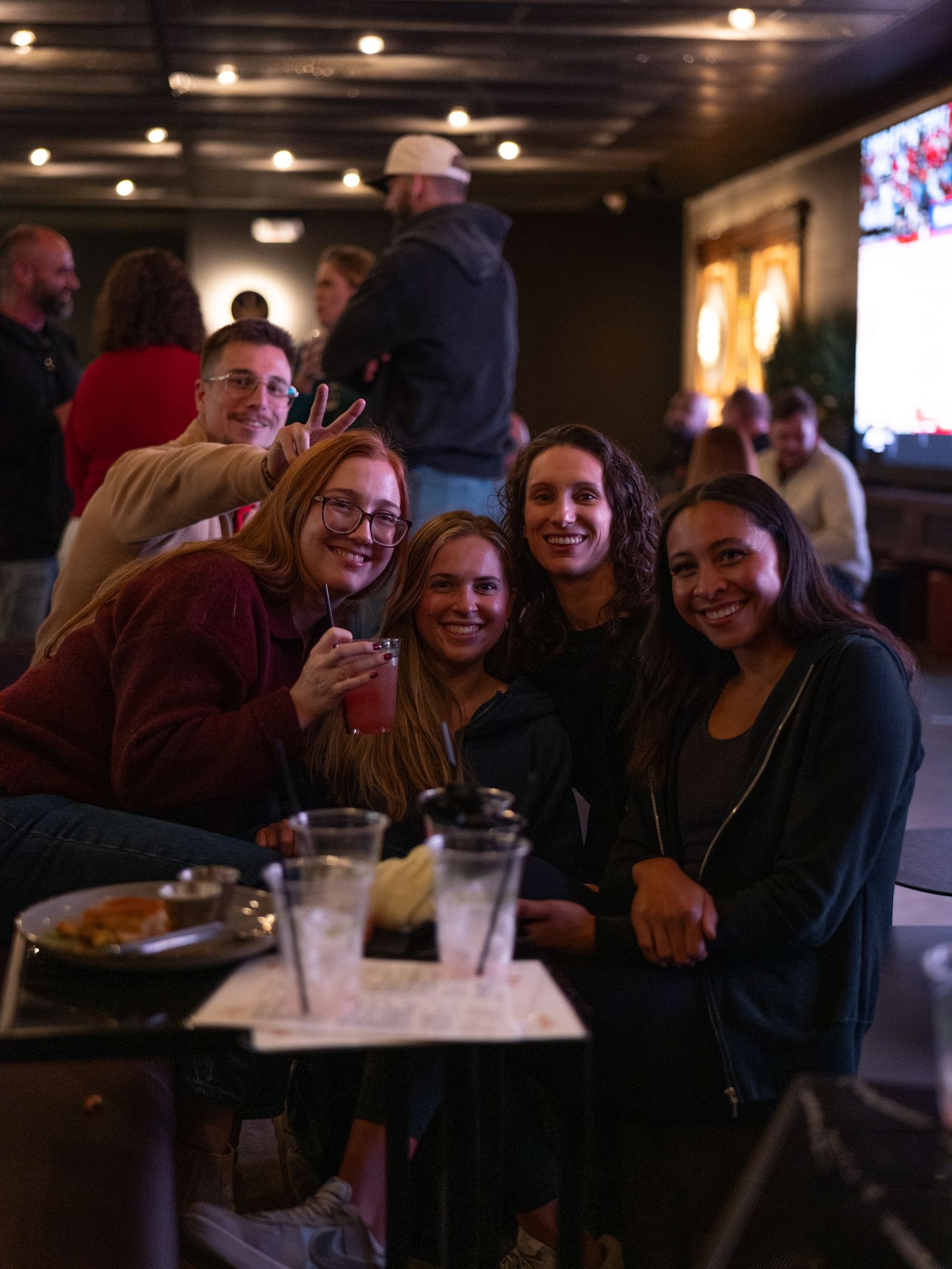 Friends enjoying drinks and laughter together at a dimly lit bar or restaurant.