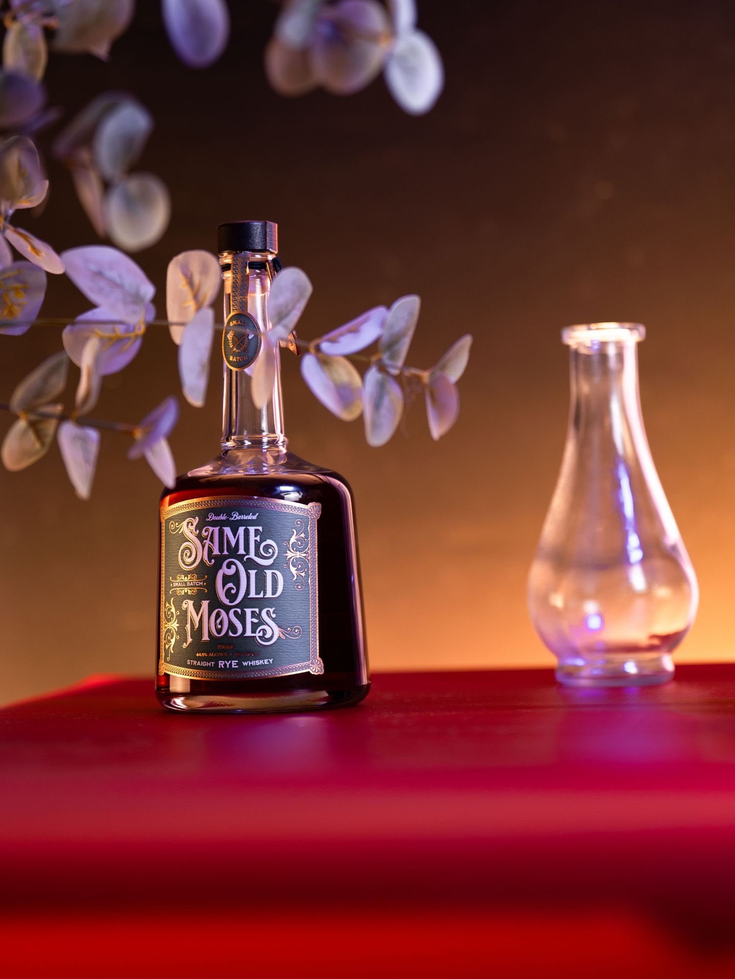 A bottle of Old Roses liquor with glowing glass tulip in moody lighting on red velvet surface.