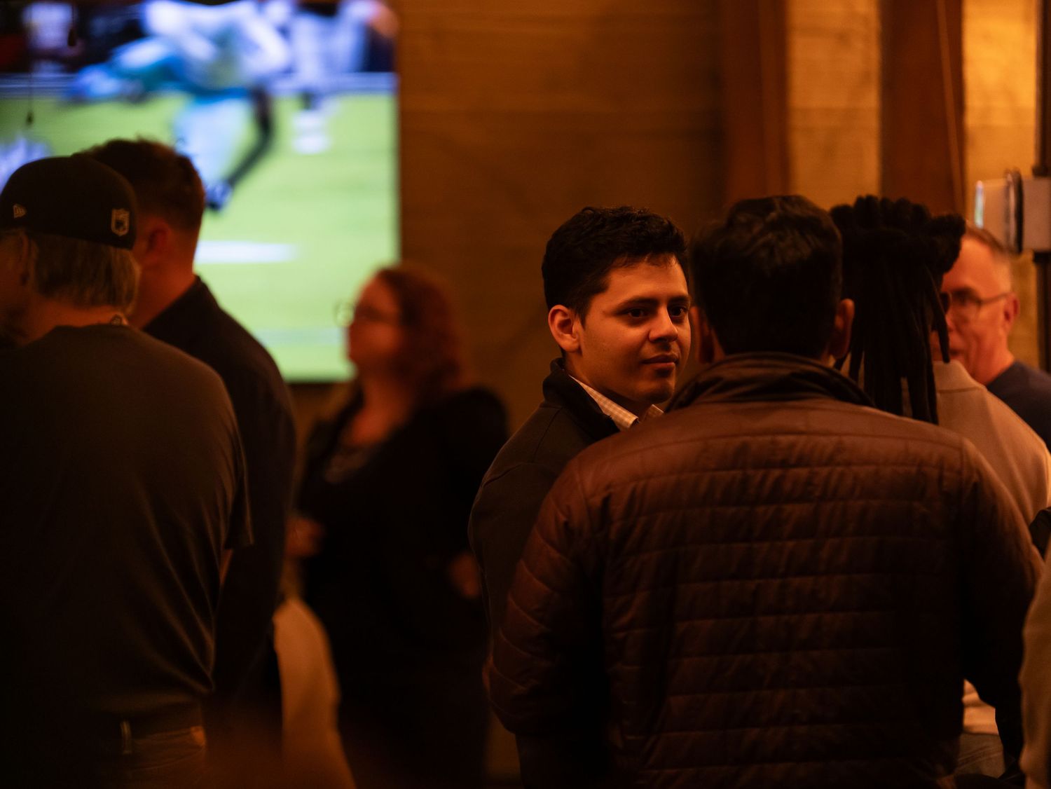 A dark collage of people watching sports at a bar with multiple TV screens showing games.