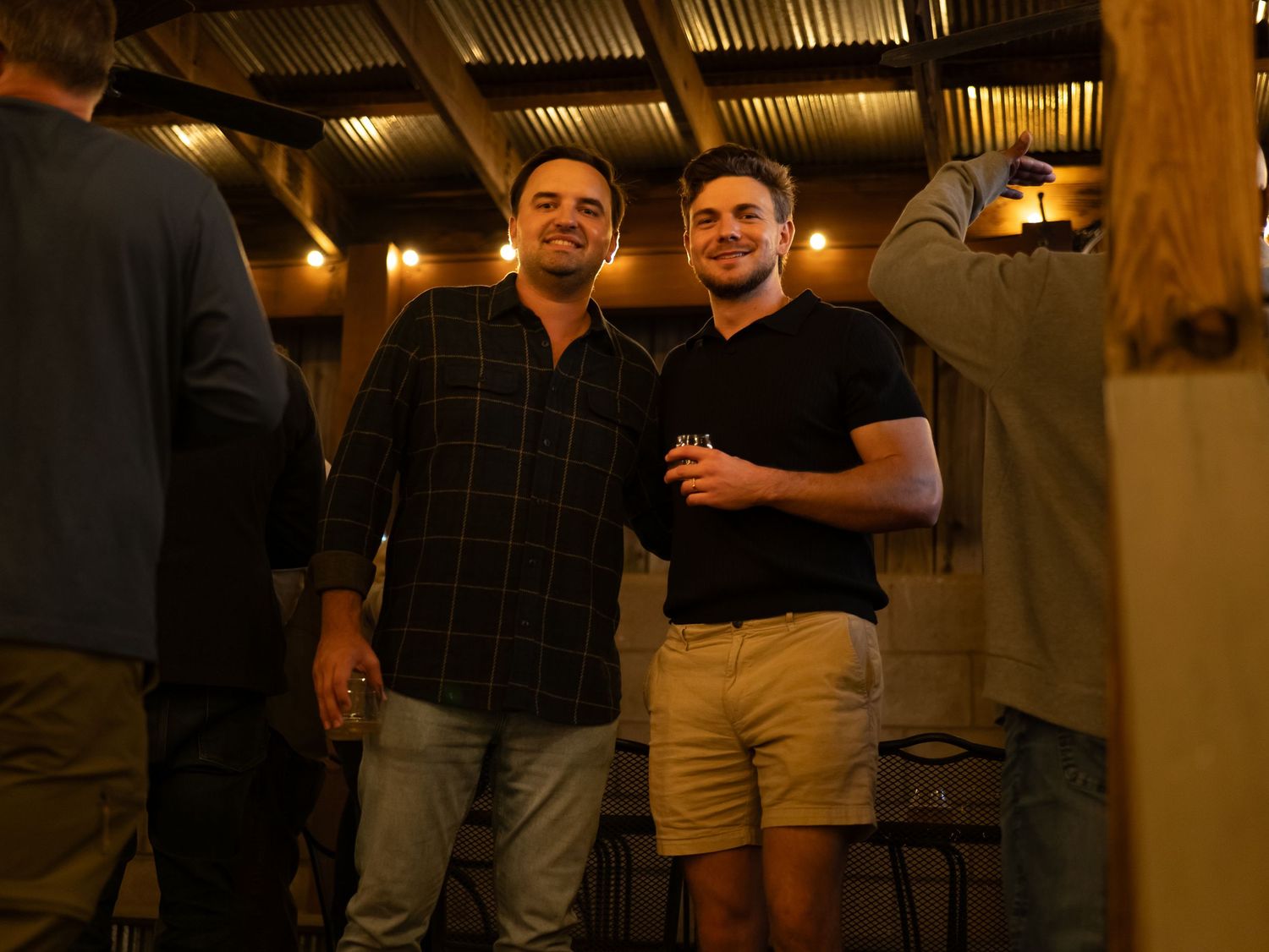 A group of friends pose together at a rustic indoor venue with wooden beams and warm lighting.