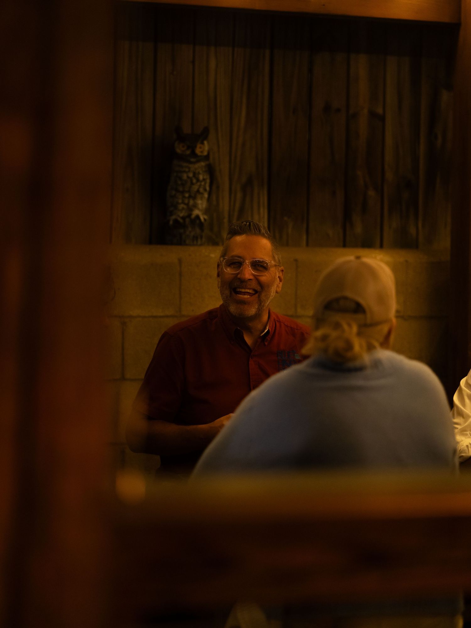 A person in a blue shirt sits at a wooden table in a dimly lit room with warm ambient lighting.