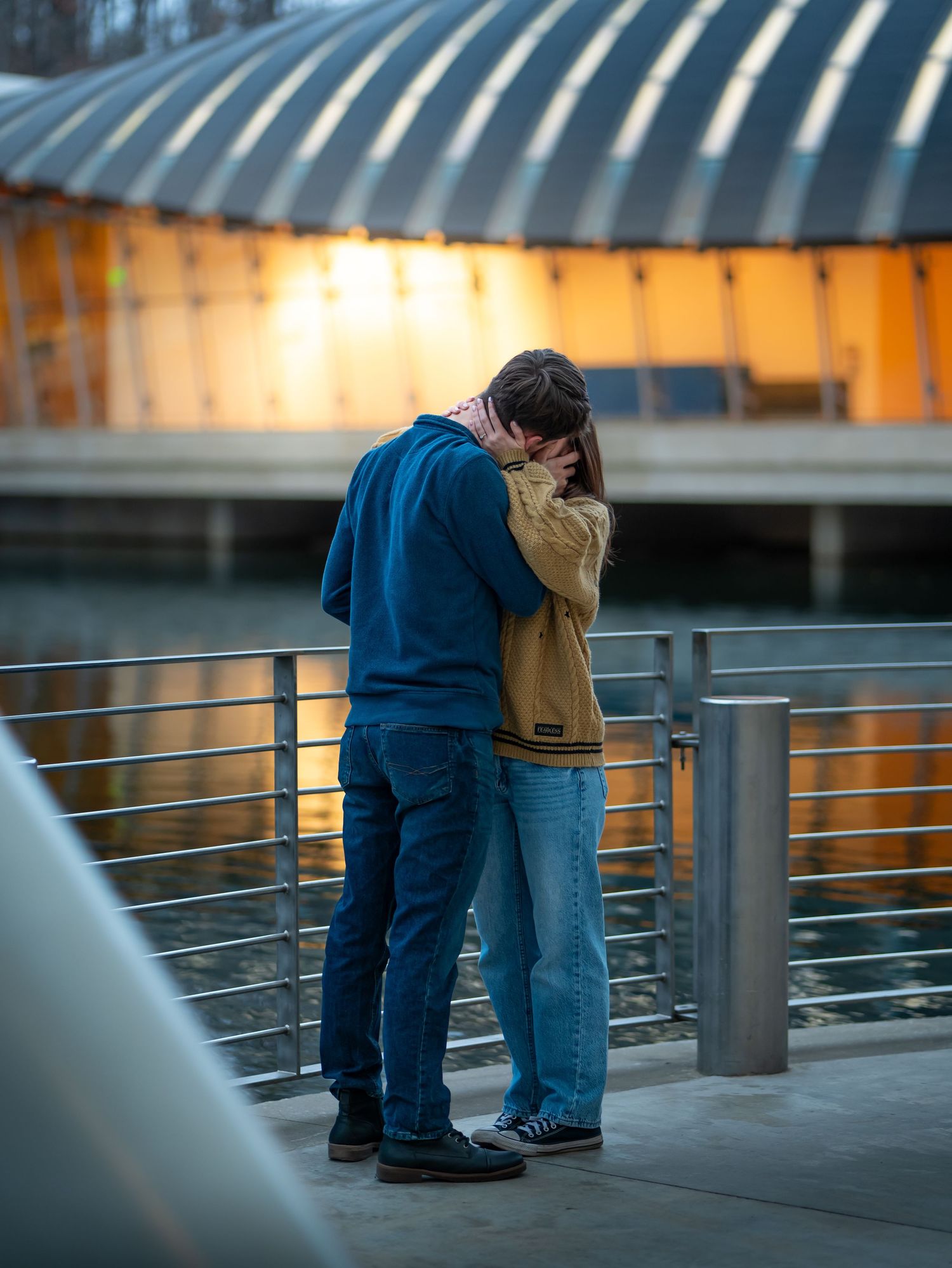 Two people lean against a railing at sunset creating a silhouette against the warm glowing sky.