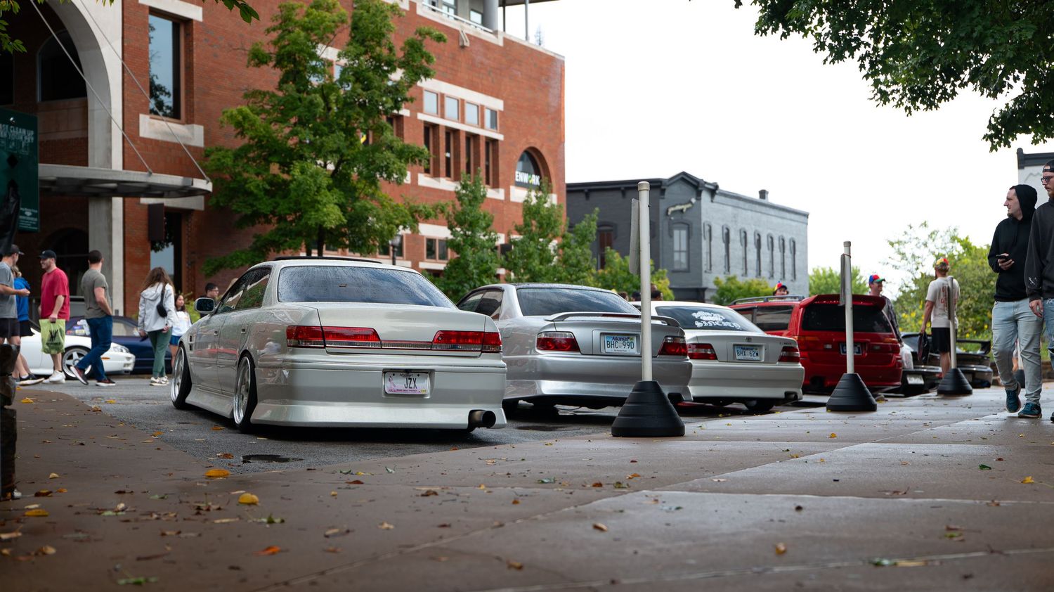 Urban street scene with brick buildings, parked cars, and pedestrians on sidewalk.