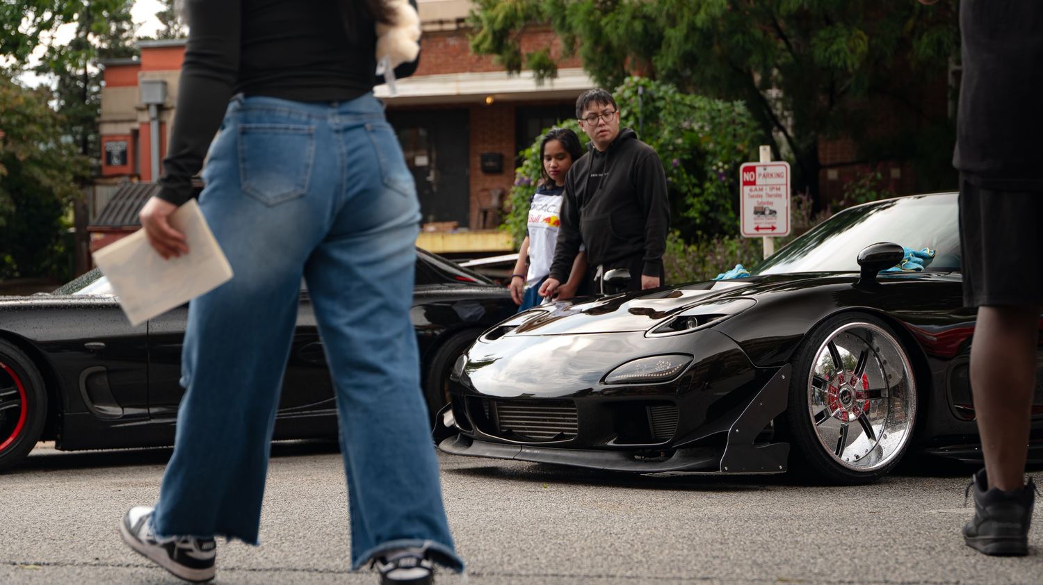 Black sports car with custom wheels parked on street during car meet.