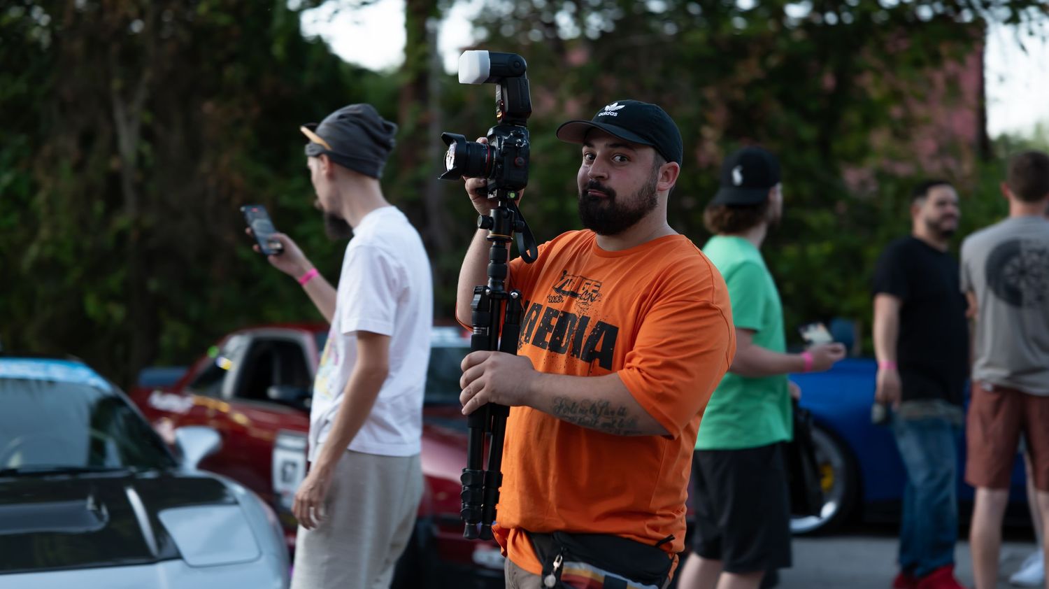 Outdoor car meet during sunset with enthusiasts gathering around modified vehicles.