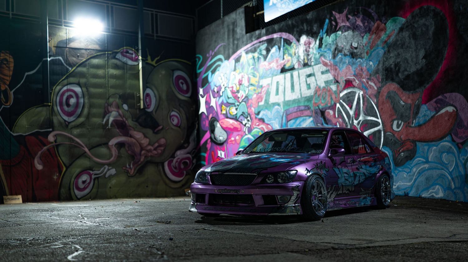 Urban wall covered in colorful graffiti art illuminated by bright lights at night.