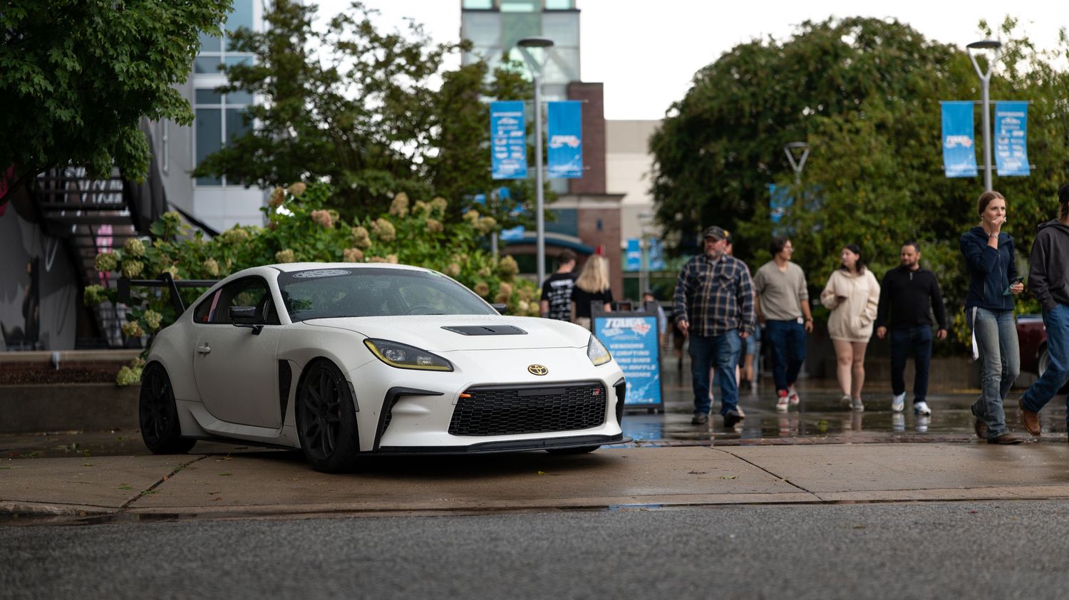 Wide angle view of a car show with spectators browsing displayed vehicles.