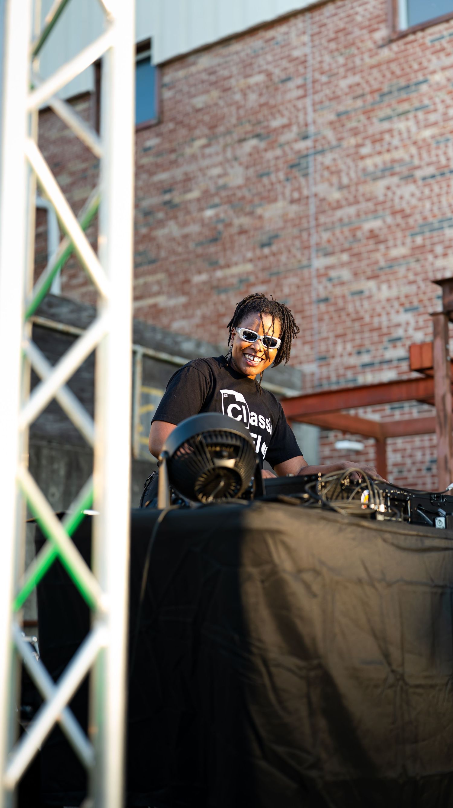 DJ equipment setup with turntables and mixer on a black-covered table against brick wall backdrop.