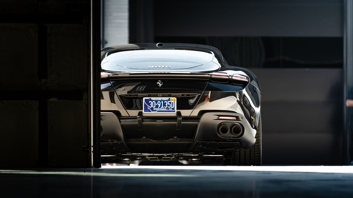 Rear view of a dark sports car showing its license plate and exhaust system.