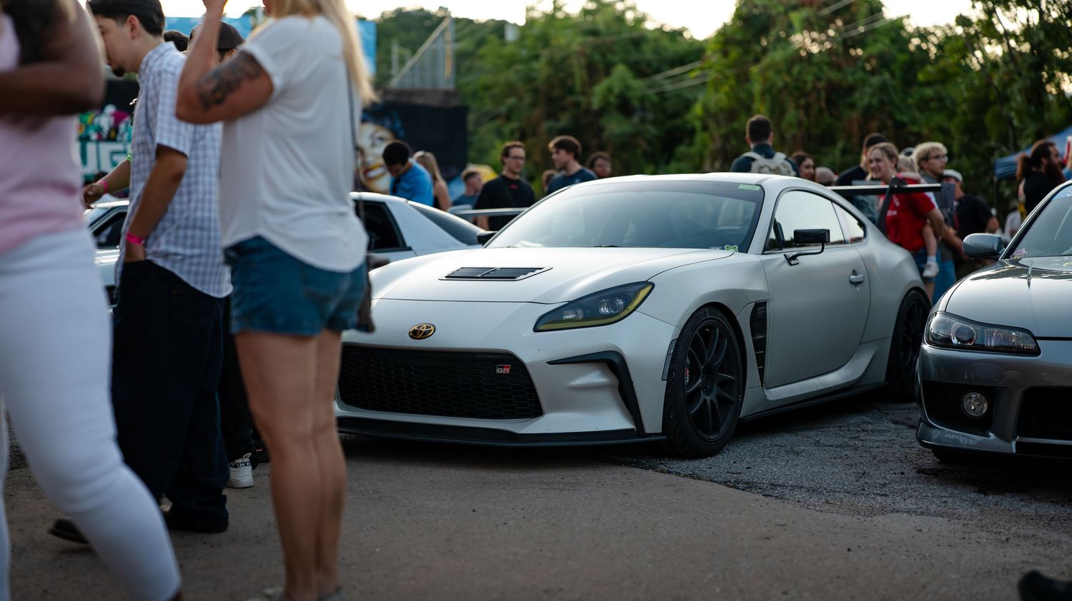 Modified sports cars lined up at a car show with spectators admiring the vehicles.