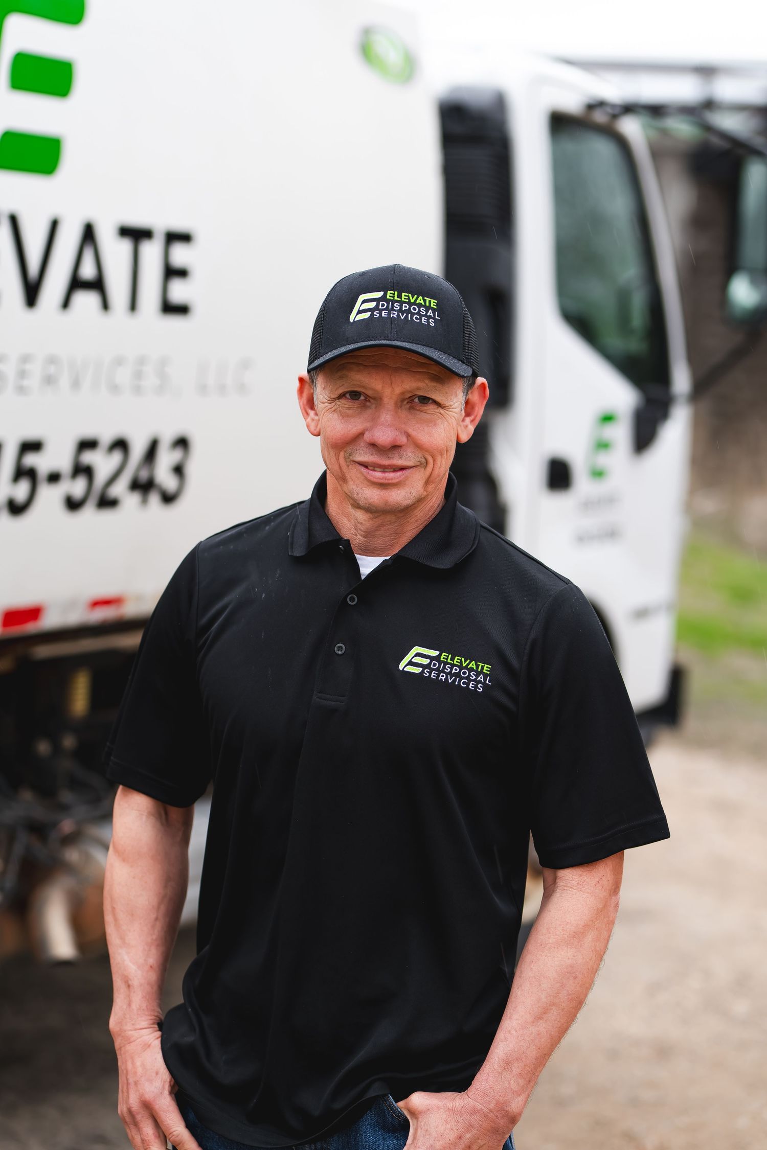 Employee in branded polo and cap poses by company trucks.