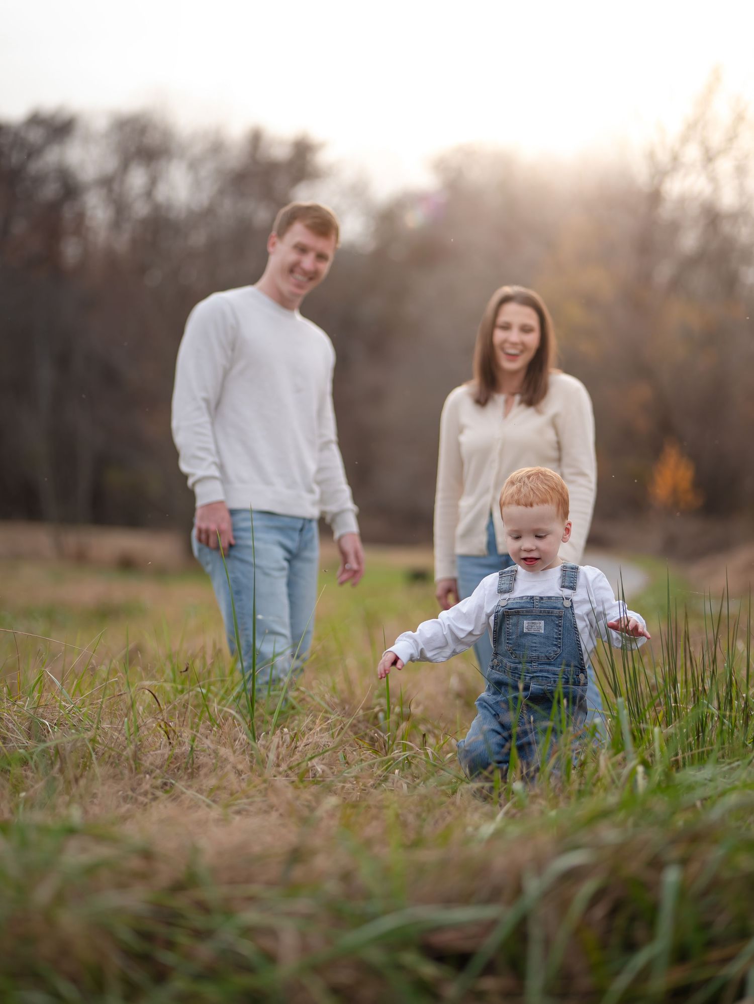 Family walking together through a golden field at sunset with tall grass in the foreground.
