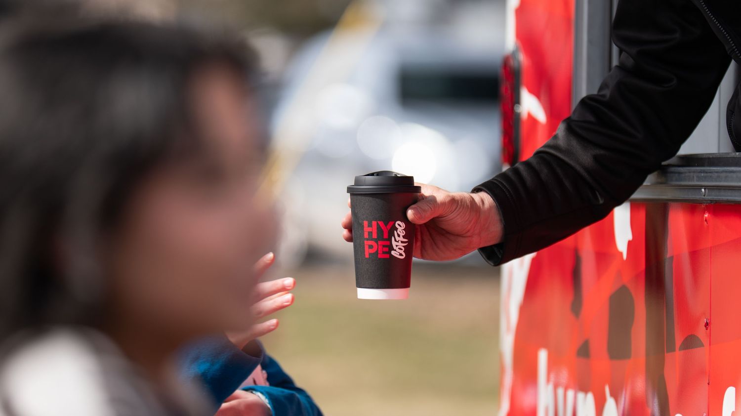 Close-up of hands exchanging coffee cups with red branding.