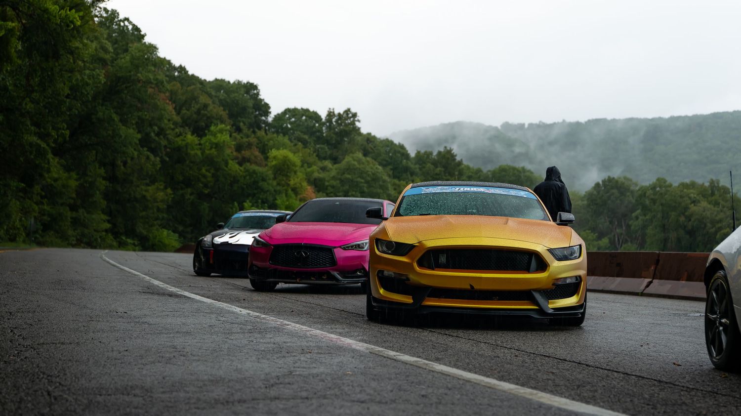 Performance cars displayed on a scenic mountain overlook during daytime.