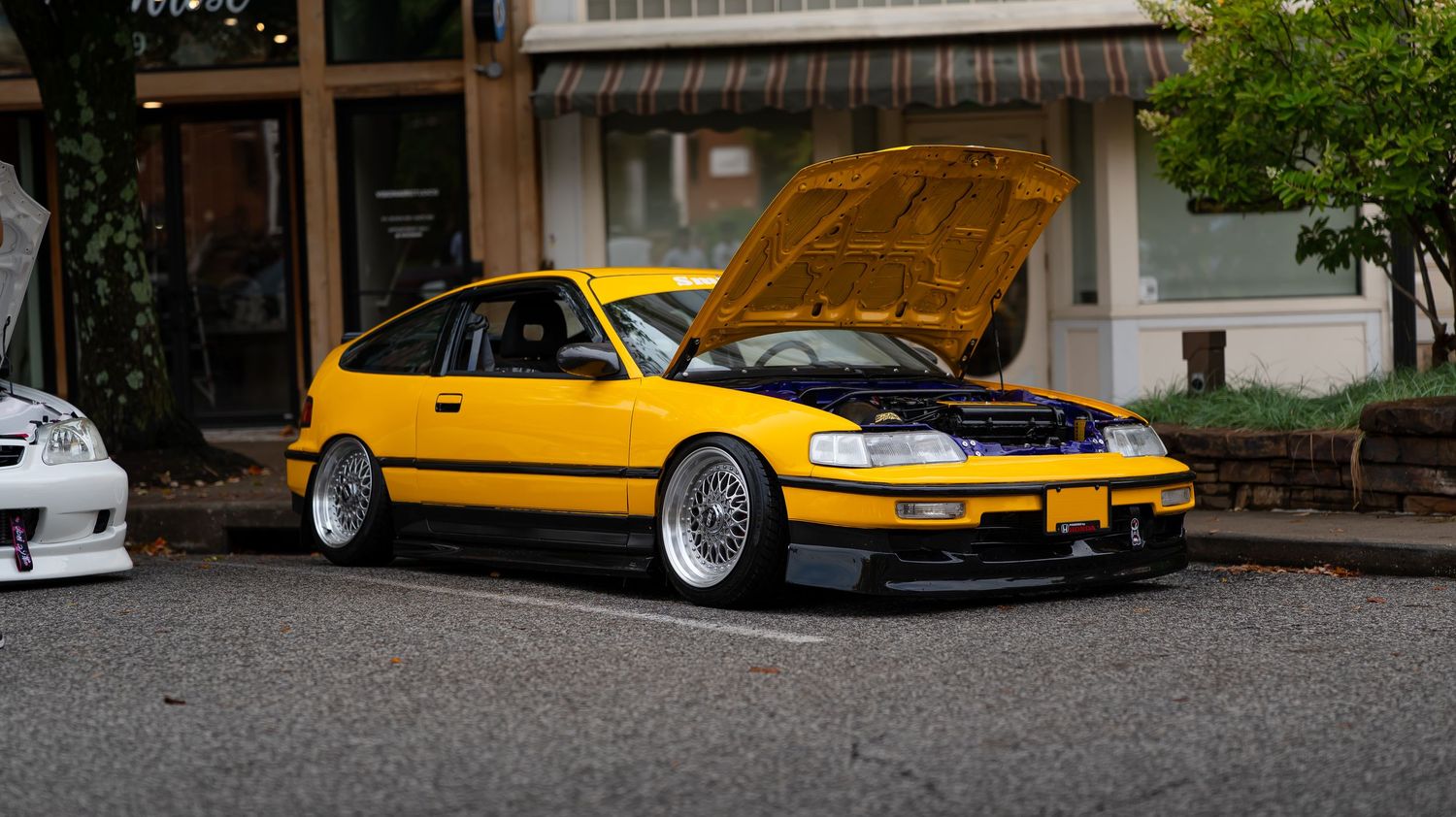 Yellow modified sports car parked alongside other custom vehicles at a car meet.