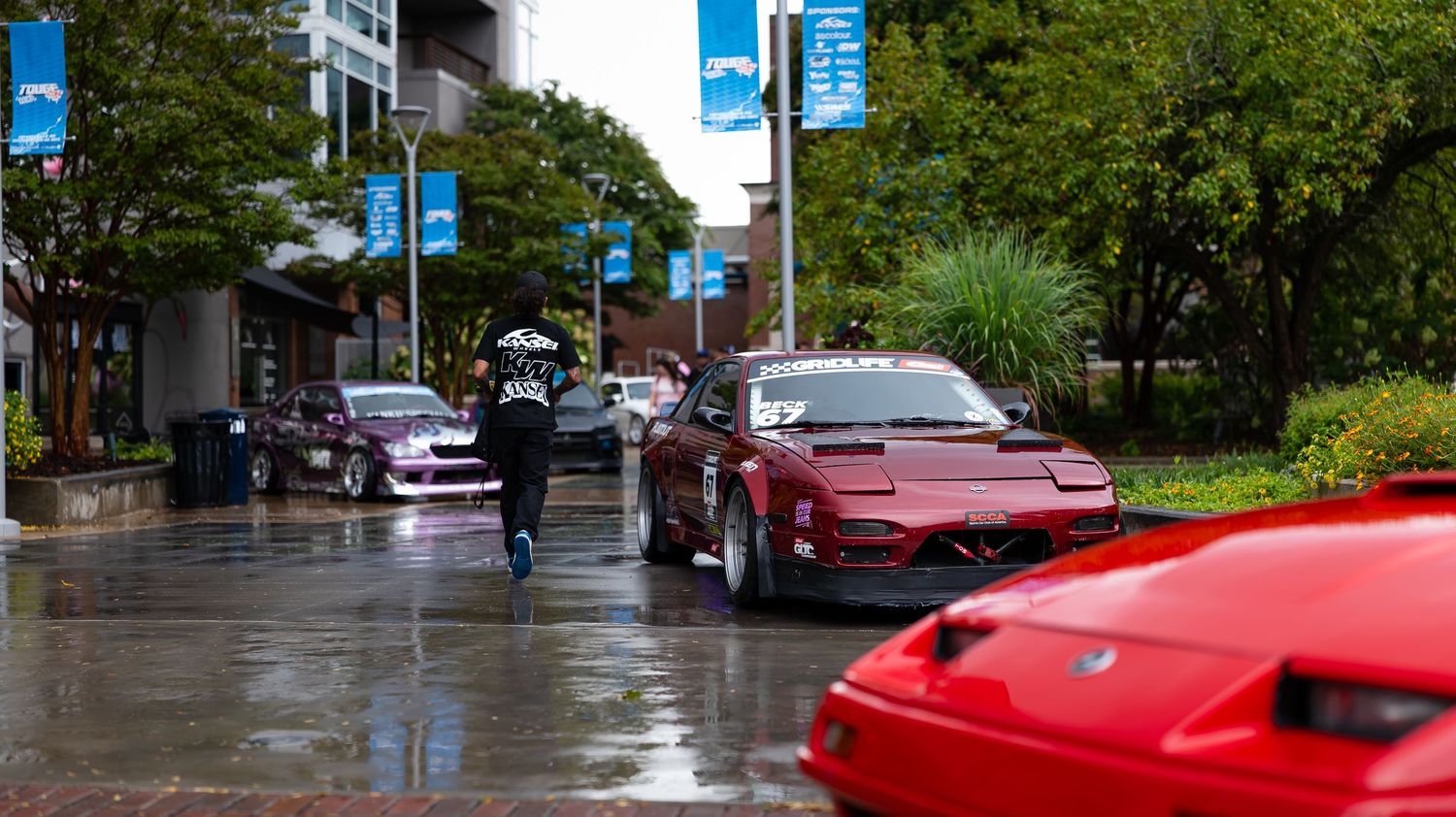 Line of sports cars parked along a wet city street with blue banners.