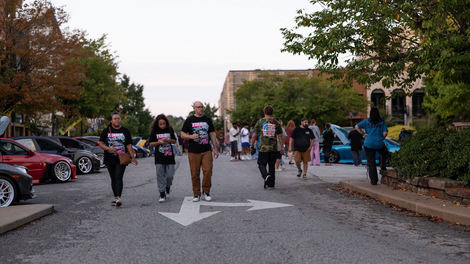 Wide view of parking area with cars and attendees at dusk gathering.