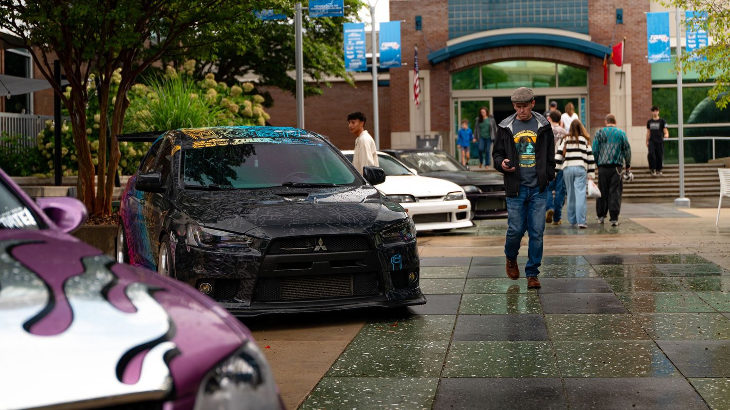 Urban street scene with parked vehicles and pedestrians near brick buildings.