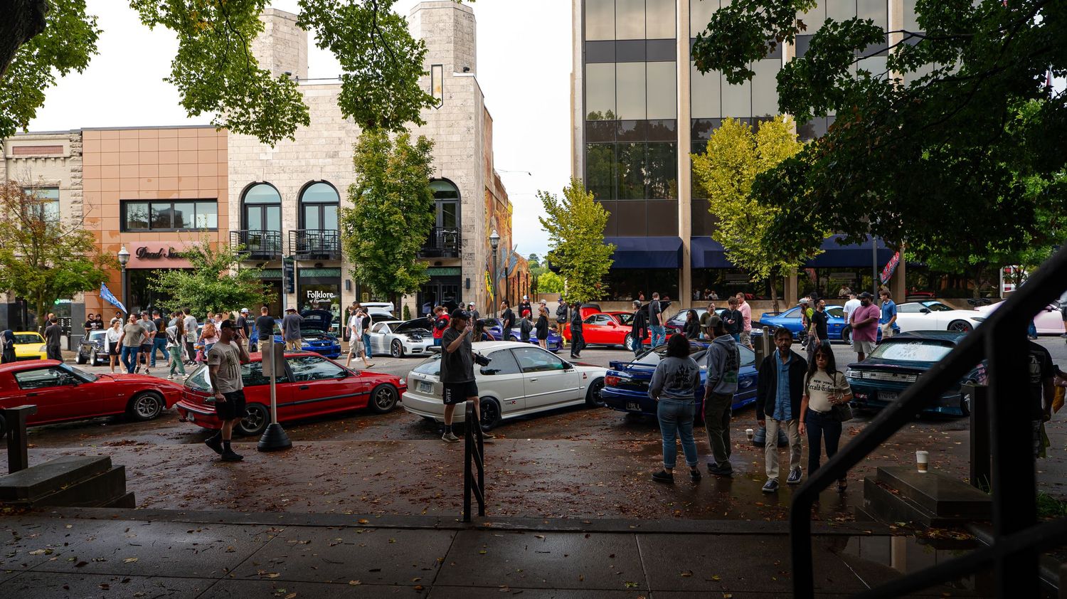 Street view of brick buildings and parked cars with green trees lining the sidewalk.