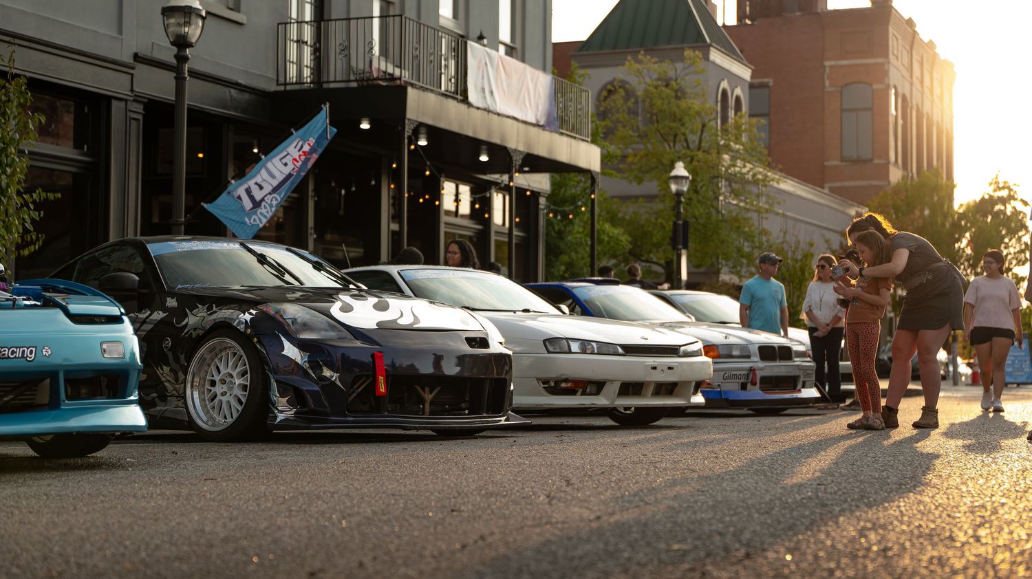 Panoramic view of a city street with vintage architecture and parked cars at sunset.