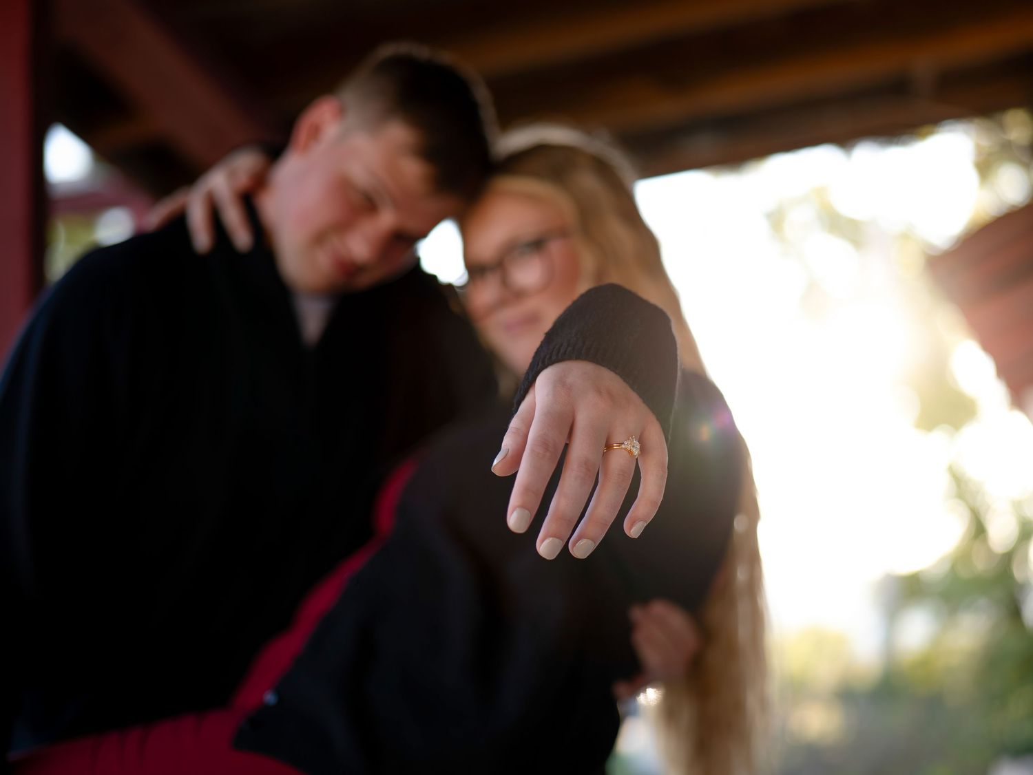 An intimate engagement photo showing hands and a ring in warm sunlight.